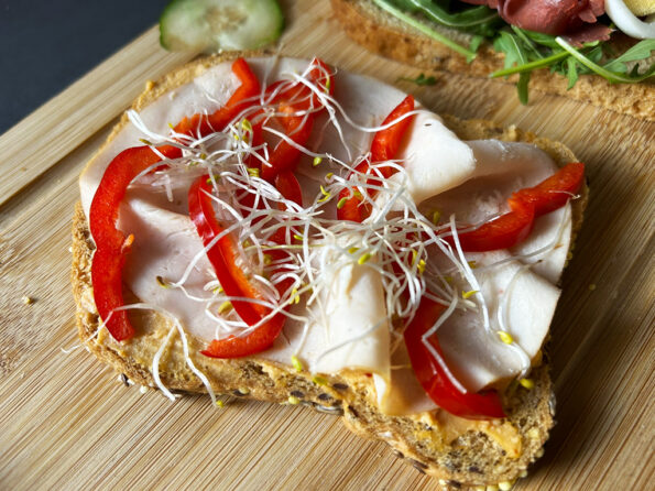 Glutenvrije open sandwich met hummus, gebraden kipfilet, rode punt paprika en alfalfa